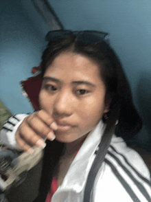 a blurry picture of a woman wearing sunglasses and a white adidas jacket