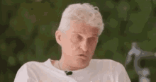 a man with white hair is wearing a white t-shirt and a microphone on his neck .