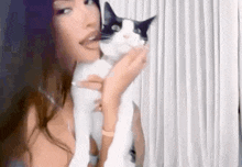 a woman is holding a black and white cat in her arms in front of a curtain .