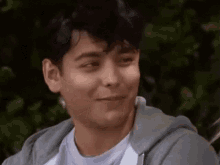 a young man wearing a grey hoodie and a white t-shirt is smiling .