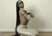 a woman with long hair is kneeling down wearing sunglasses