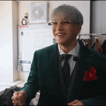 a man wearing glasses and a green suit smiles for the camera