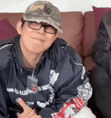 a man wearing glasses and a hat is sitting on a couch holding a cell phone .