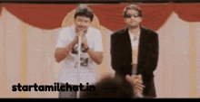 two men are standing in front of a microphone with the website starttamilchat.in visible in the corner