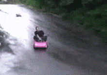 a person is driving a pink toy car on a road