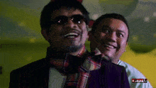 a man wearing sunglasses and a scarf laughs next to another man with the word full on the bottom left