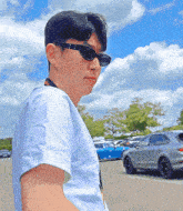 a man wearing sunglasses stands in a parking lot with cars parked in the background