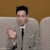 a man in a suit and tie is sitting on a couch making a funny face .