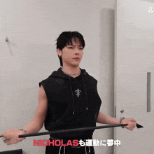 a man in a black sleeveless hoodie is holding a bar with nicholas written in red