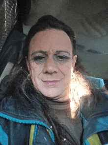 a woman in a blue jacket is taking a selfie in a car