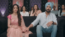 a man and woman are sitting on a couch holding hands