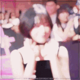 a woman is making a heart shape with her hands while holding a cell phone .