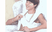 a young man is sitting in a chair wearing a white tank top and a gold chain around his neck .
