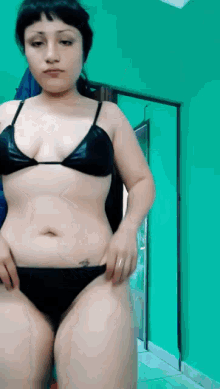 a woman in a bikini is standing in front of a green wall .