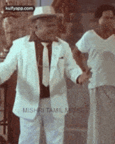 a man in a white suit and tie is standing next to a man in a hat .