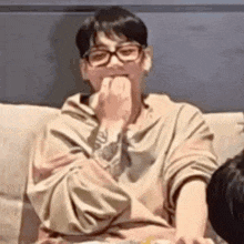 a man wearing glasses is sitting on a couch and eating a piece of food .