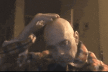 a man in a plaid shirt is shaving his head with a razor