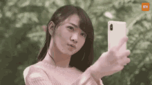 a woman is taking a selfie with her phone in a park .