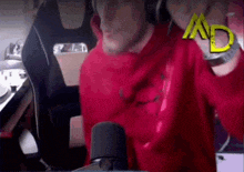 a man in a red hoodie is sitting in front of a microphone and headphones .