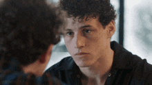 a young man with curly hair looks at his reflection in a mirror