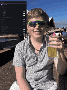 a young man wearing sunglasses holds up a glass of beer