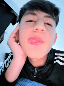 a young man with his tongue sticking out wearing a black adidas shirt