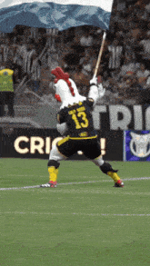 a chicken mascot is holding a flag while wearing a jersey with the number 13 on it