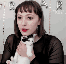 a woman is holding a kitten in front of balloons that say " rar "