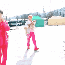 a man in pink pants is holding a small dog in his arms .