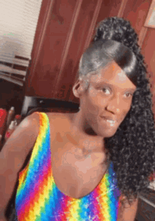 a woman wearing a rainbow tank top and a ponytail is sitting in a chair .