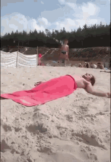 a man laying on a beach with a pink towel on his back
