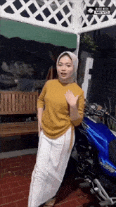 a woman wearing a hijab is standing in front of a blue motorcycle that says made with miyo