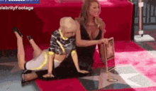 two women are kneeling on a red carpet and one is holding a book ..