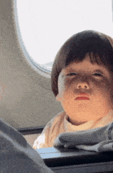 a young boy looks out of an airplane window with his eyes closed