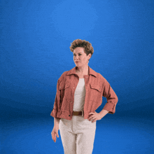 a woman in a pink jacket and white shirt is reaching up with her hand