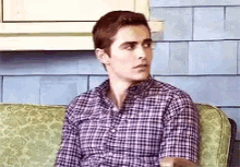a man is sitting on a couch wearing a plaid shirt .