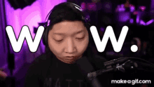 a man wearing headphones is standing in front of a microphone with the words wow written on his face .