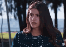 a girl in a blue jacket with white polka dots is standing in a park