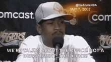 a man is talking into a microphone while wearing a baseball cap .