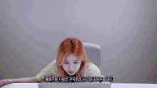 a woman sits at a desk looking at a laptop with korean writing on the bottom