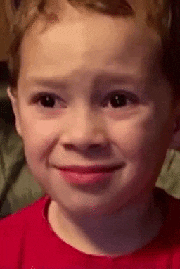 a close up of a child 's face with a red shirt on making a funny face .