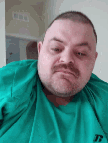 a man with a beard wearing a green shirt with the letter t on it