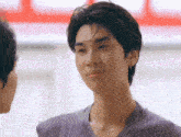 a young man in a purple shirt is looking at another man in a room .
