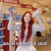 a woman with red hair is holding a bag of candy and a bottle of water in a store .