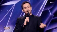 a man in a suit singing into a microphone with a mask awards logo in the background