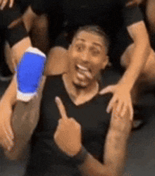 a man in a black shirt is giving a thumbs up while sitting on the floor .