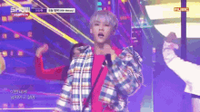 a man in a plaid jacket stands on a stage in front of a sign that says show champion music