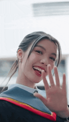 a girl in a graduation cap and gown is smiling and waving