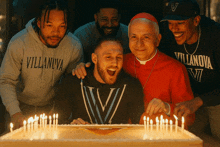 a man wearing a villanova sweatshirt stands in front of a cake with lit candles