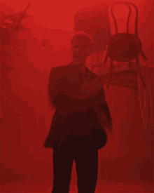 a man in a suit and tie is dancing in front of a red background